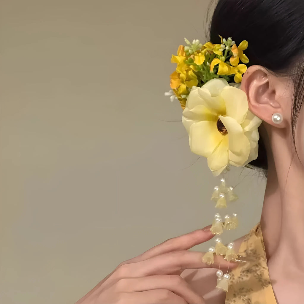 Decorative hair clip with pearls and a long yellow flower tassel on a white background.