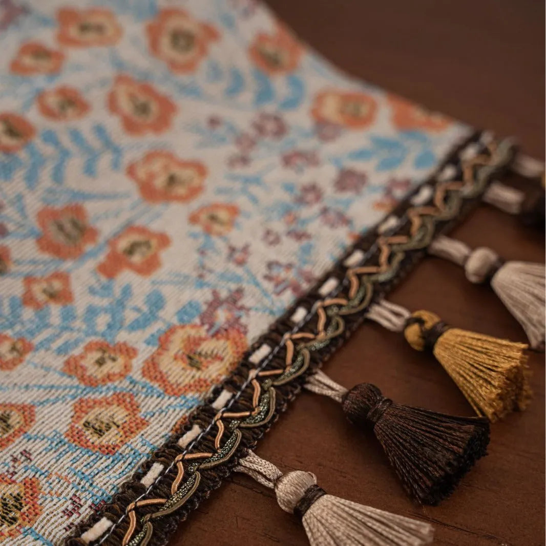 Beige Jacquard table runner with floral leaf pattern and long tassel fringe on a wooden table.
