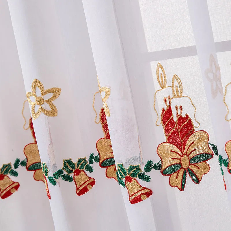 Pair of white Christmas curtains with red and green embroidered snowflakes, shown hanging in a window.