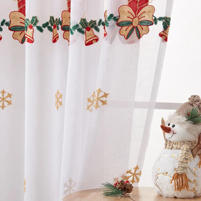 Pair of white Christmas curtains with red and green embroidered snowflakes, shown hanging in a window.