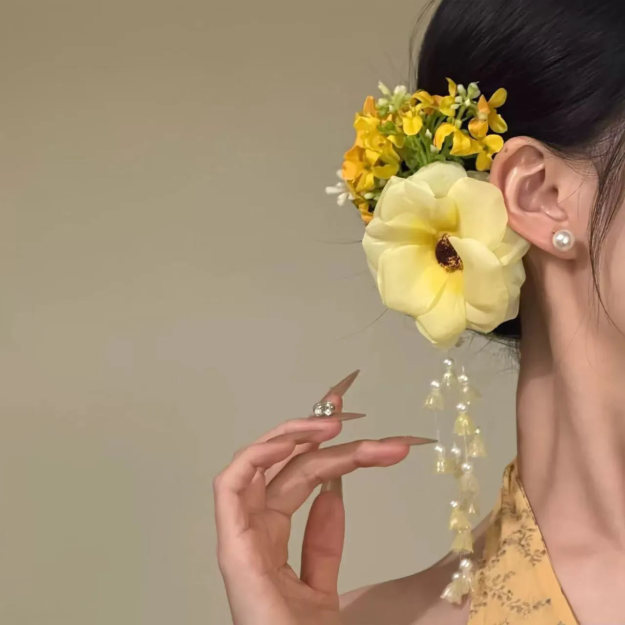 Decorative hair clip with pearls and a long yellow flower tassel on a white background.