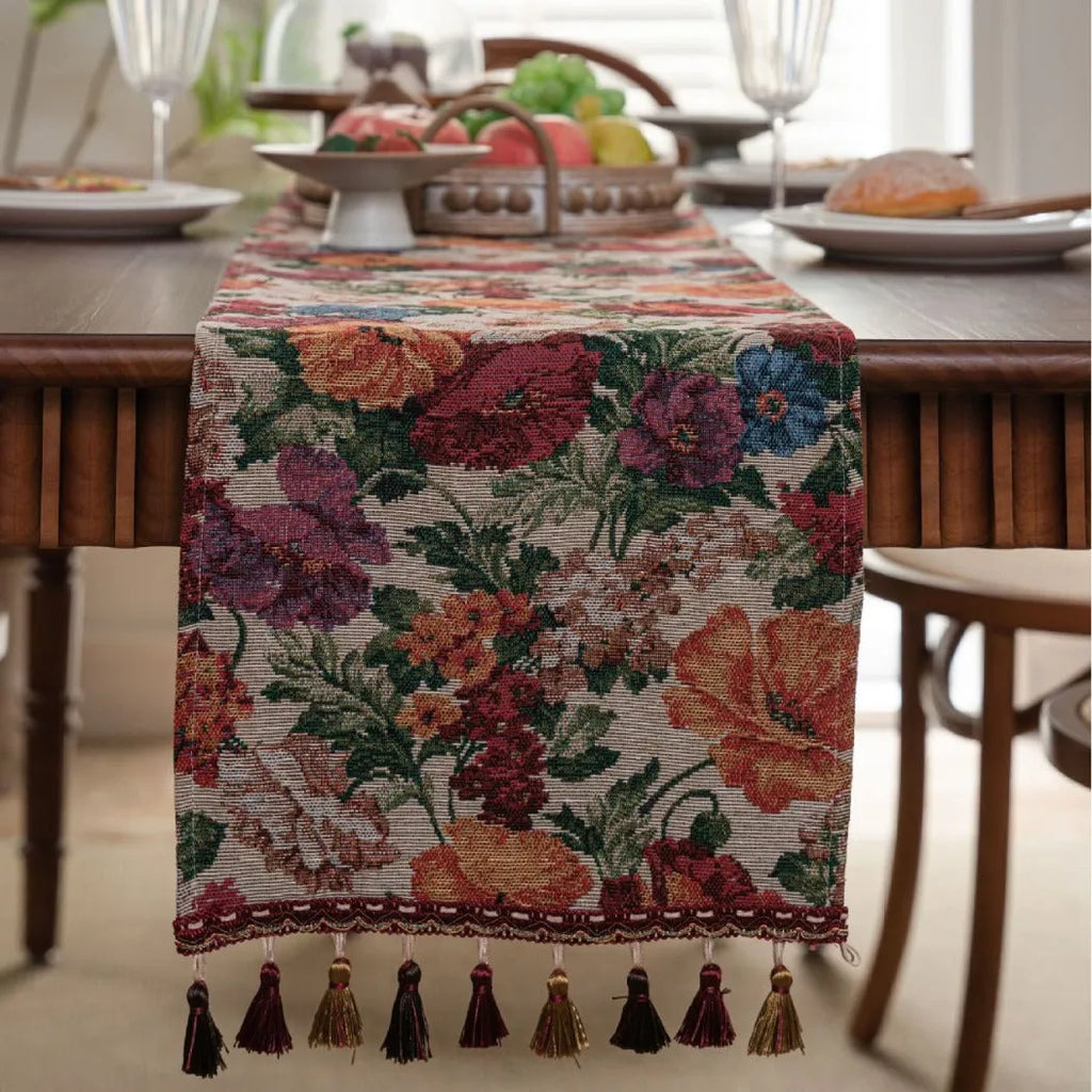 Beige Jacquard table runner with floral leaf pattern and long tassel fringe on a wooden table.