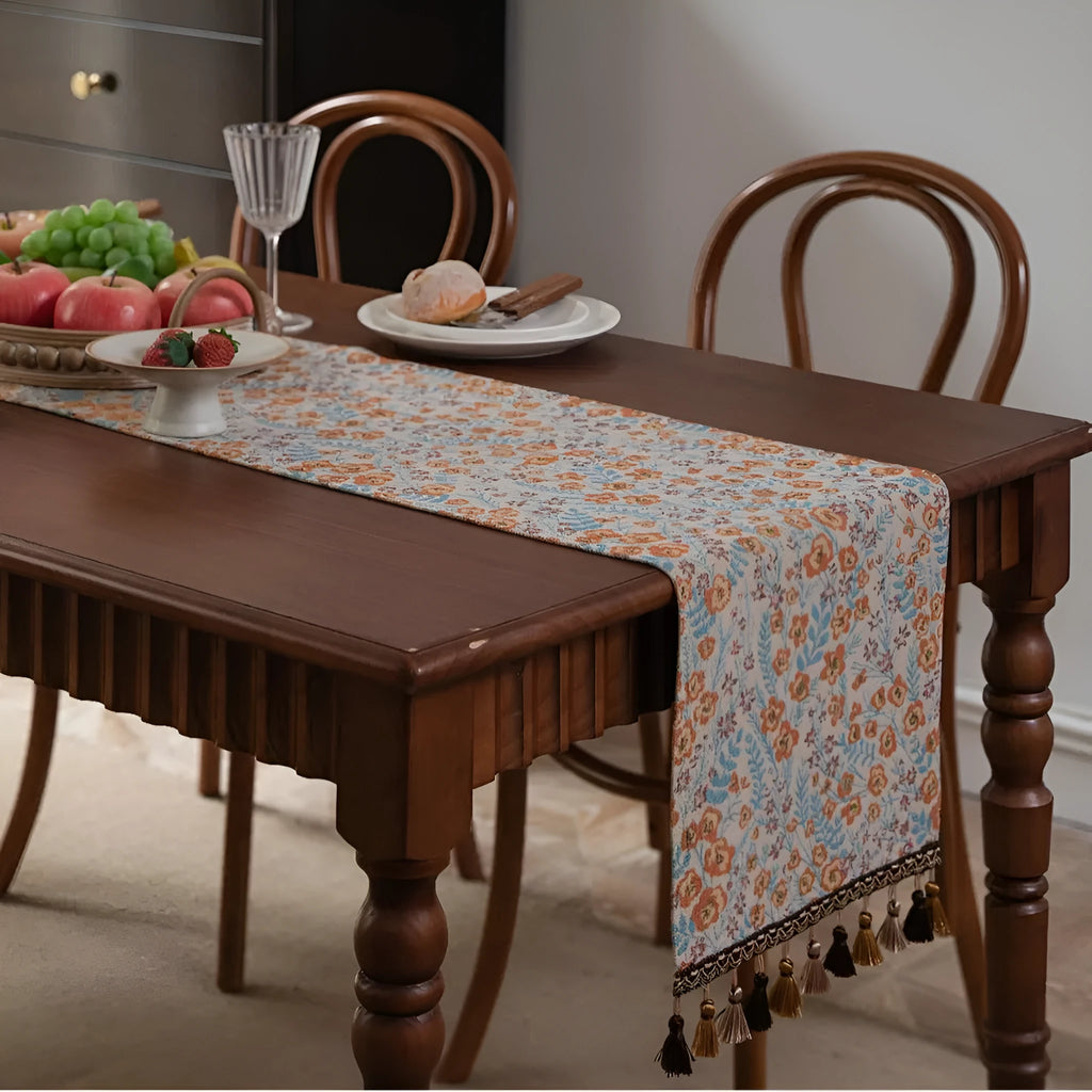 Beige Jacquard table runner with floral leaf pattern and long tassel fringe on a wooden table.