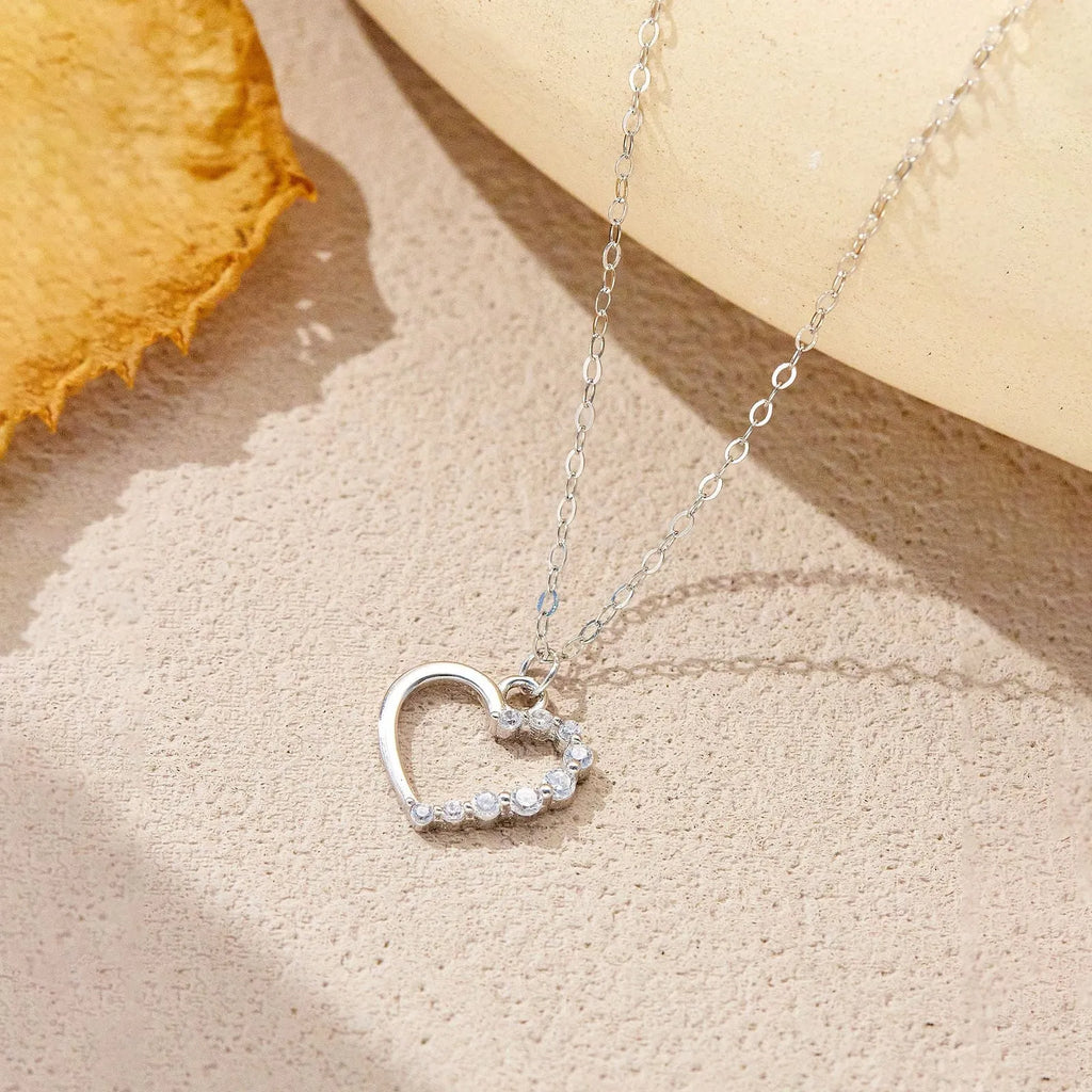 Close-up of a hollow heart-shaped sterling silver pendant on an oval chain, shown in both gold and white gold plated finishes.