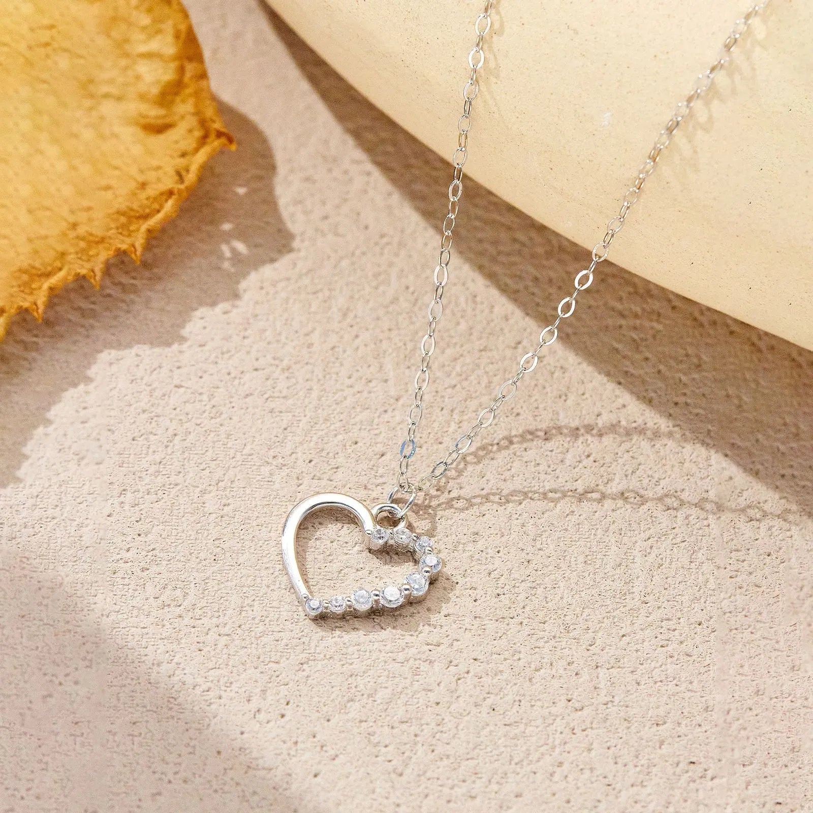 Close-up of a hollow heart-shaped sterling silver pendant on an oval chain, shown in both gold and white gold plated finishes.