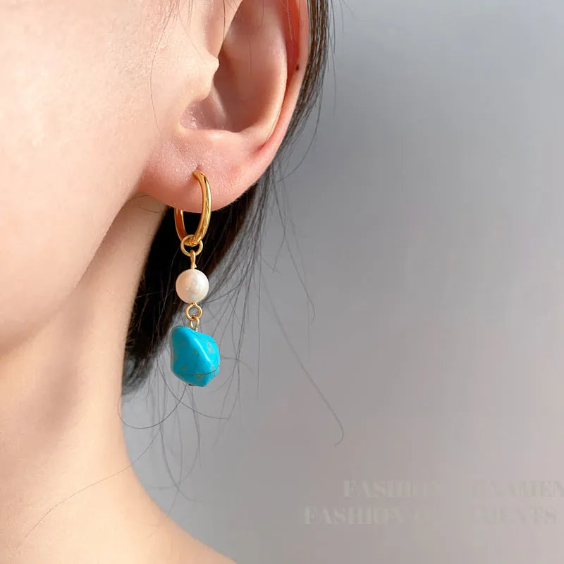 A pair of geometric turquoise and cultured pearl ear clips on a copper setting.