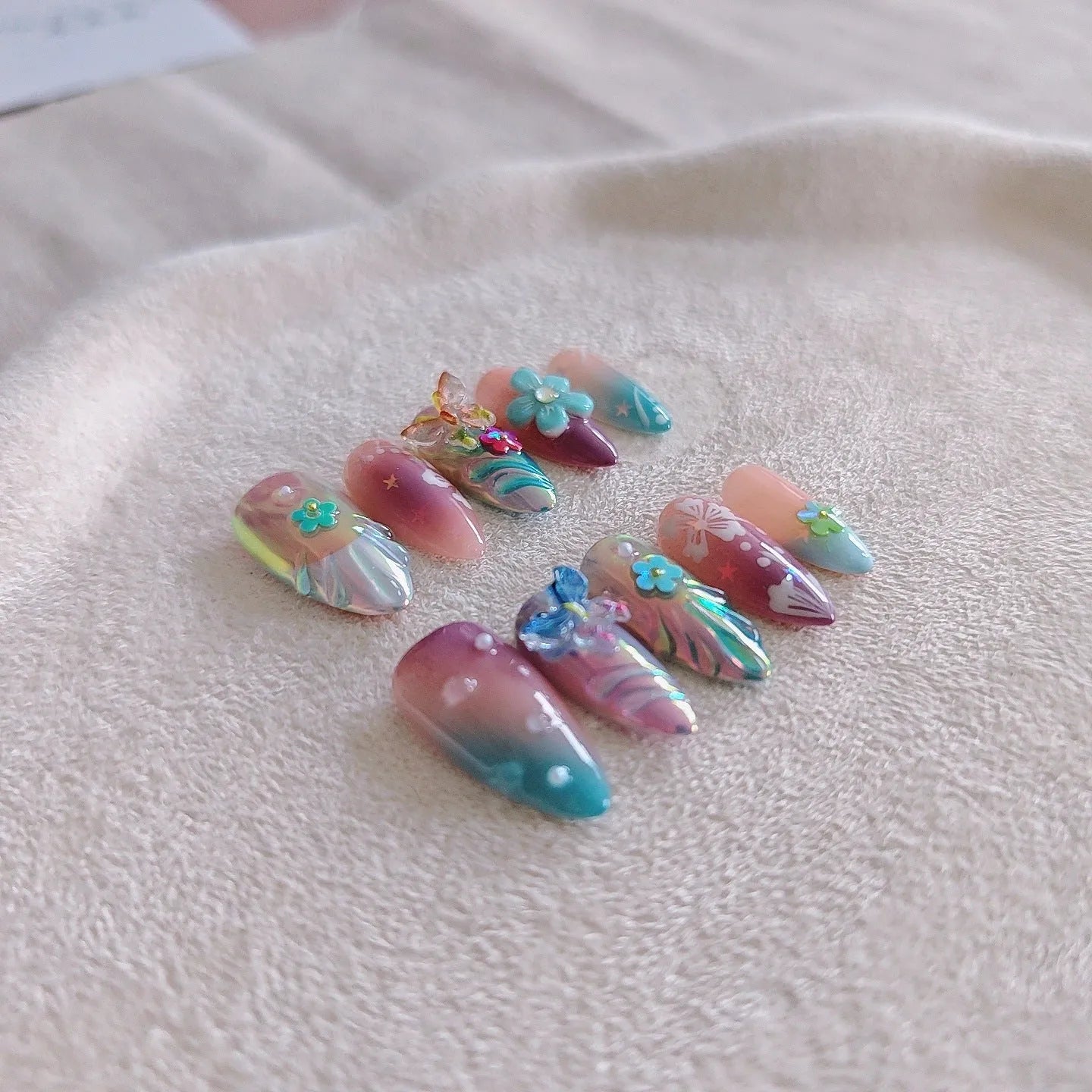 Handmade floral and butterfly nail art sculptures for manicure decoration in almond shape.