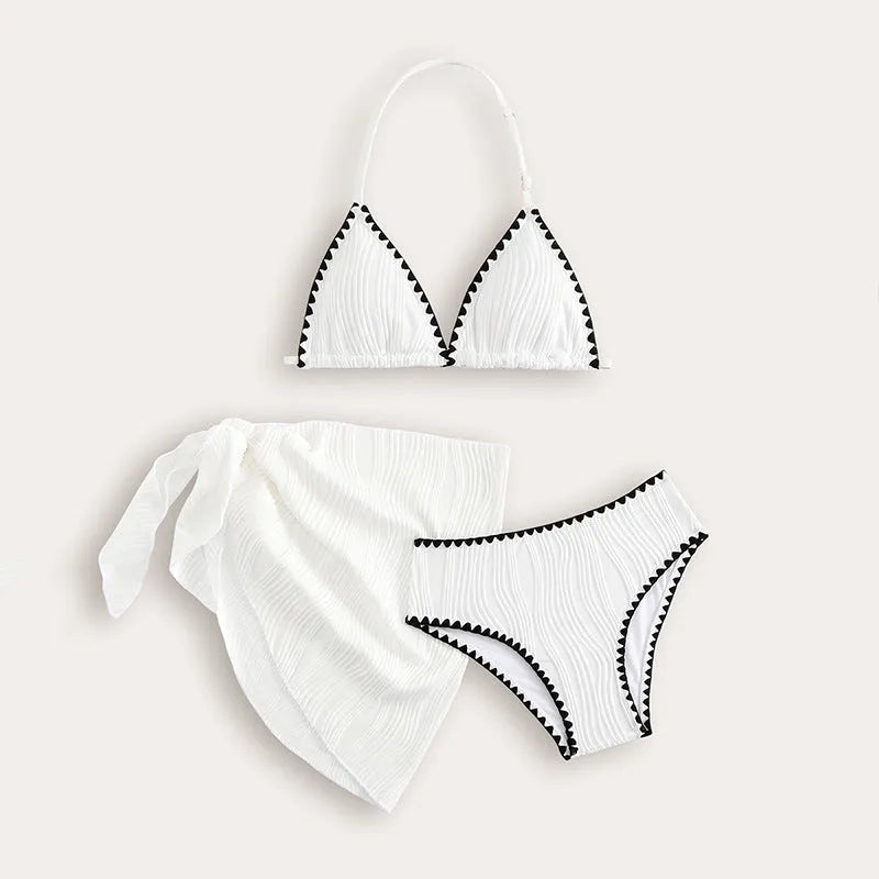 Solid white three-piece girls swimsuit set with top, pants, and skirt on a beach setting.
