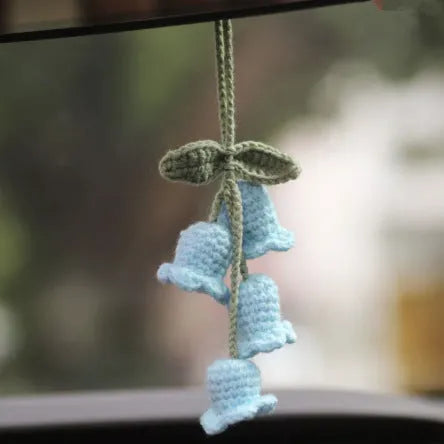 Green and white crocheted car plant decoration with hanging rope on a car dashboard.
