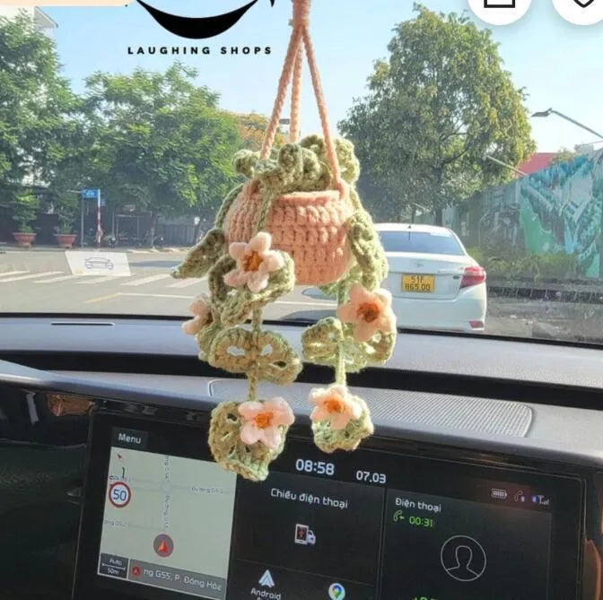 Green and white crocheted car plant decoration with hanging rope on a car dashboard.