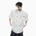 A man's loose-fit short-sleeve casual shirt with splicing detail and metal decoration on a hanger.