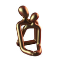 Modern minimalist resin statue of a couple in milky white or gold colour on a wooden surface.