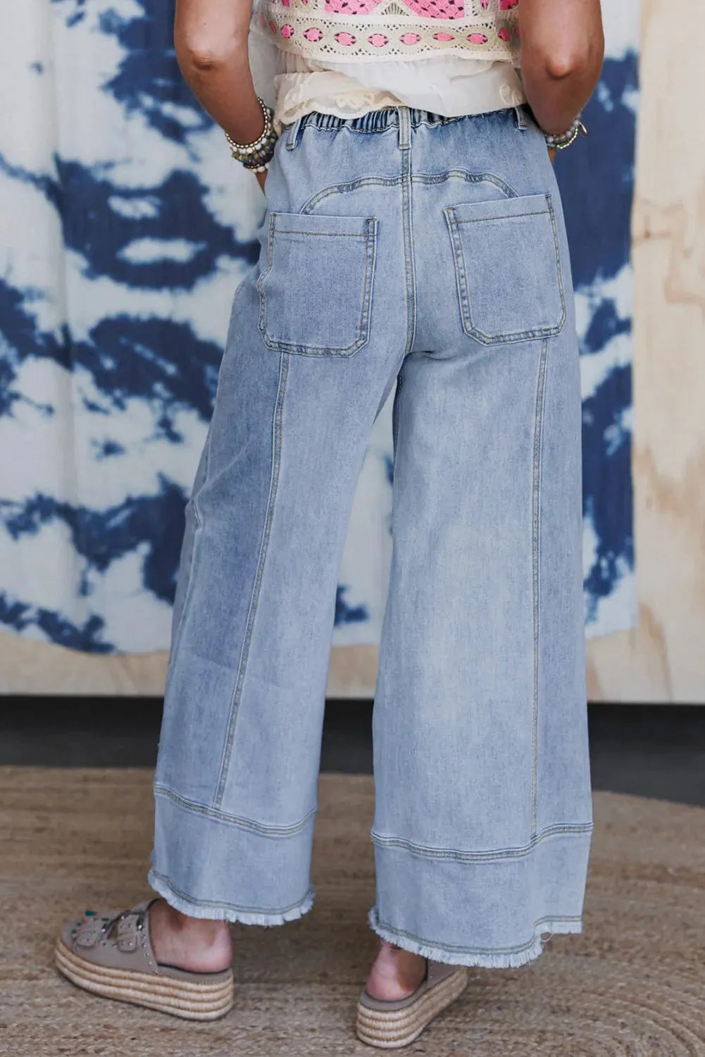 Beau blue wide leg denim trousers with a drawstring waist and raw hem detail laid flat.