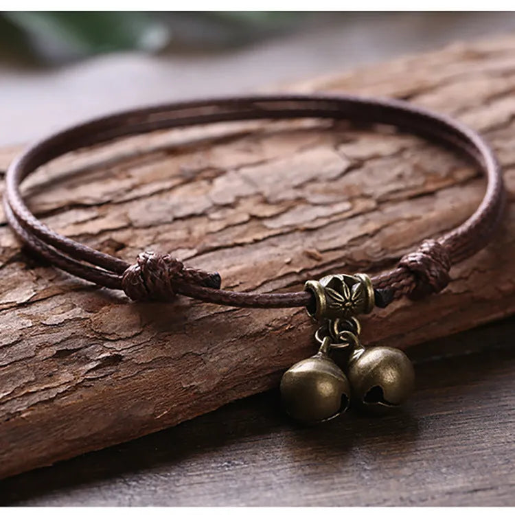 Black nylon rope dog collar with a small brass bell on a wooden background.