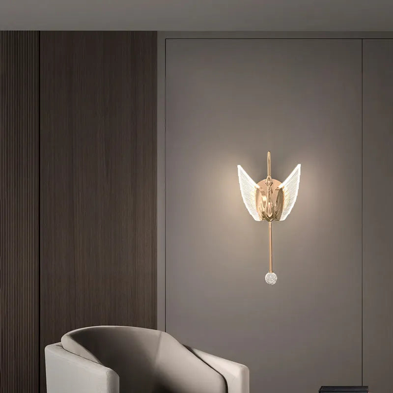 Gold swan-shaped modern minimalist wall lamp with acrylic shade on a wall.