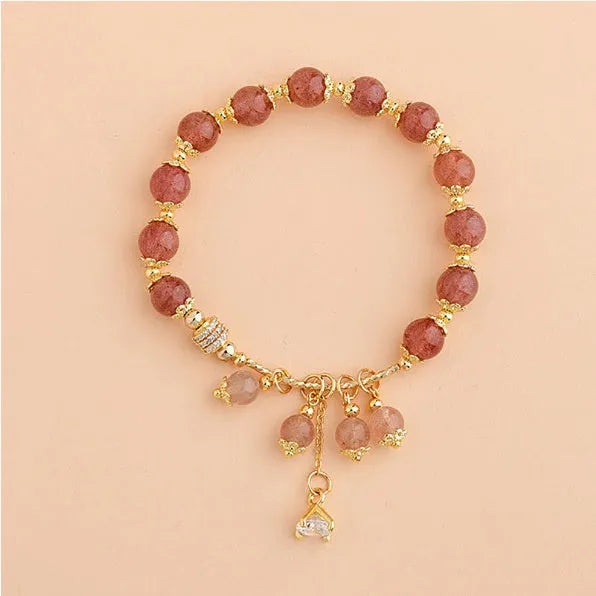 Close-up of a women's pink strawberry quartz heart bracelet with pearl details on a wrist.