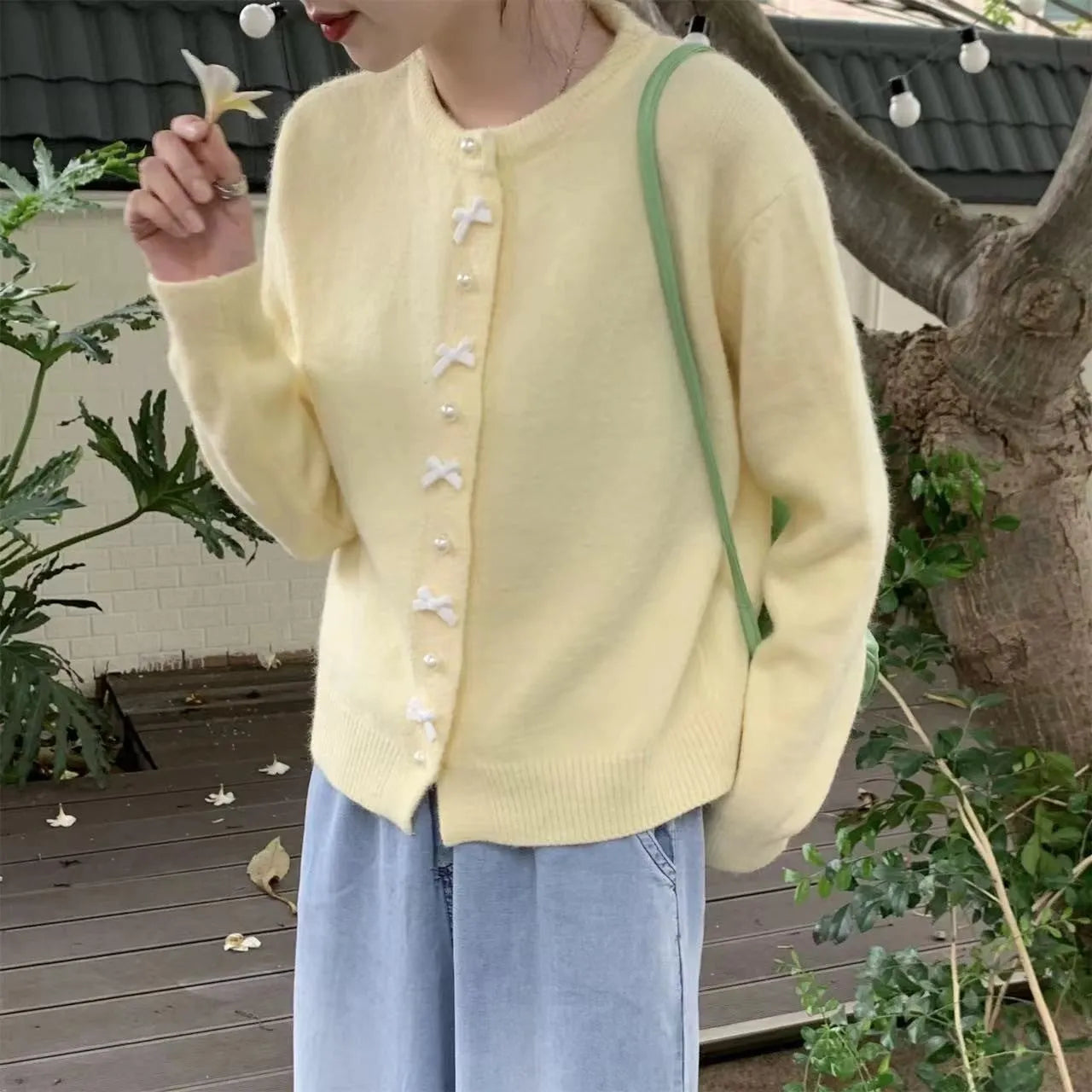 Women's light yellow cashmere acrylic cardigan with pearl buttons and a bow on the front.