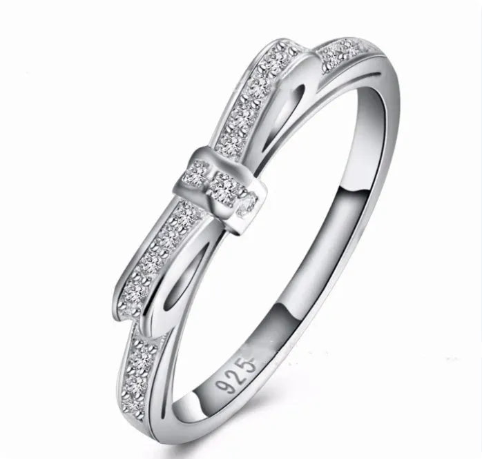 Silver bow-shaped ring with sparkling zircon crystal stones on a finger.