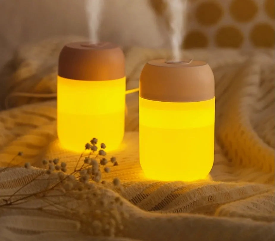 White cylindrical mini USB aromatherapy humidifier on a desk with charging cable.