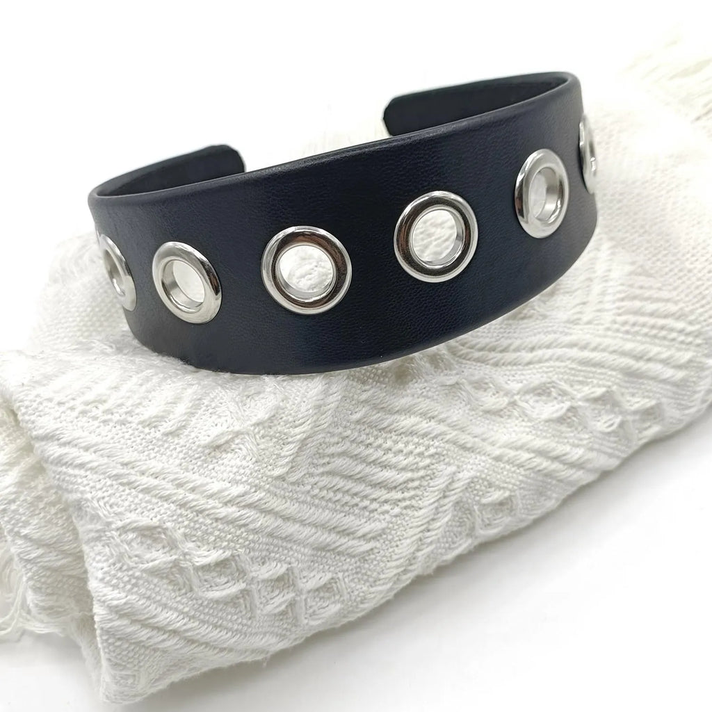Wide black faux leather headband with round, square, and dotted rivets on a white background