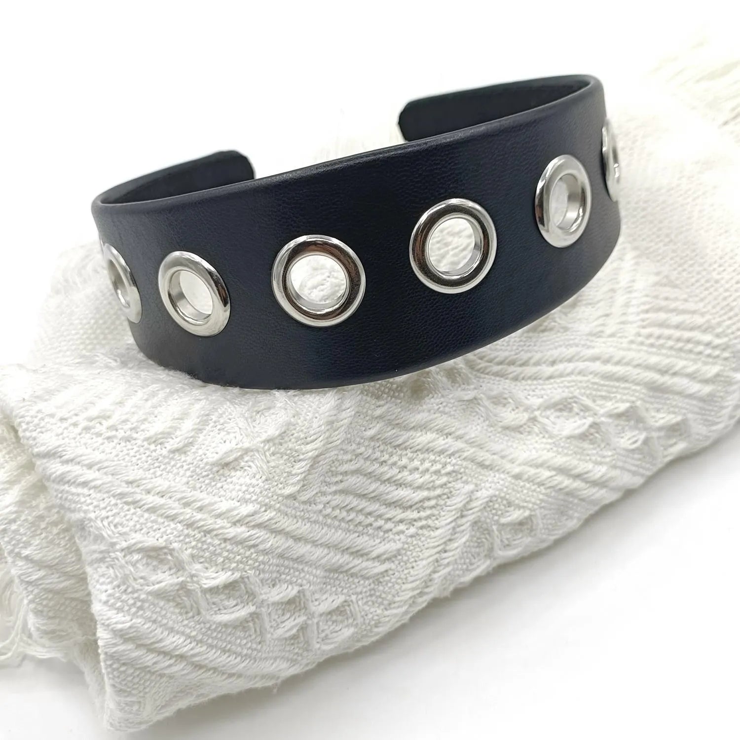 Wide black faux leather headband with round, square, and dotted rivets on a white background