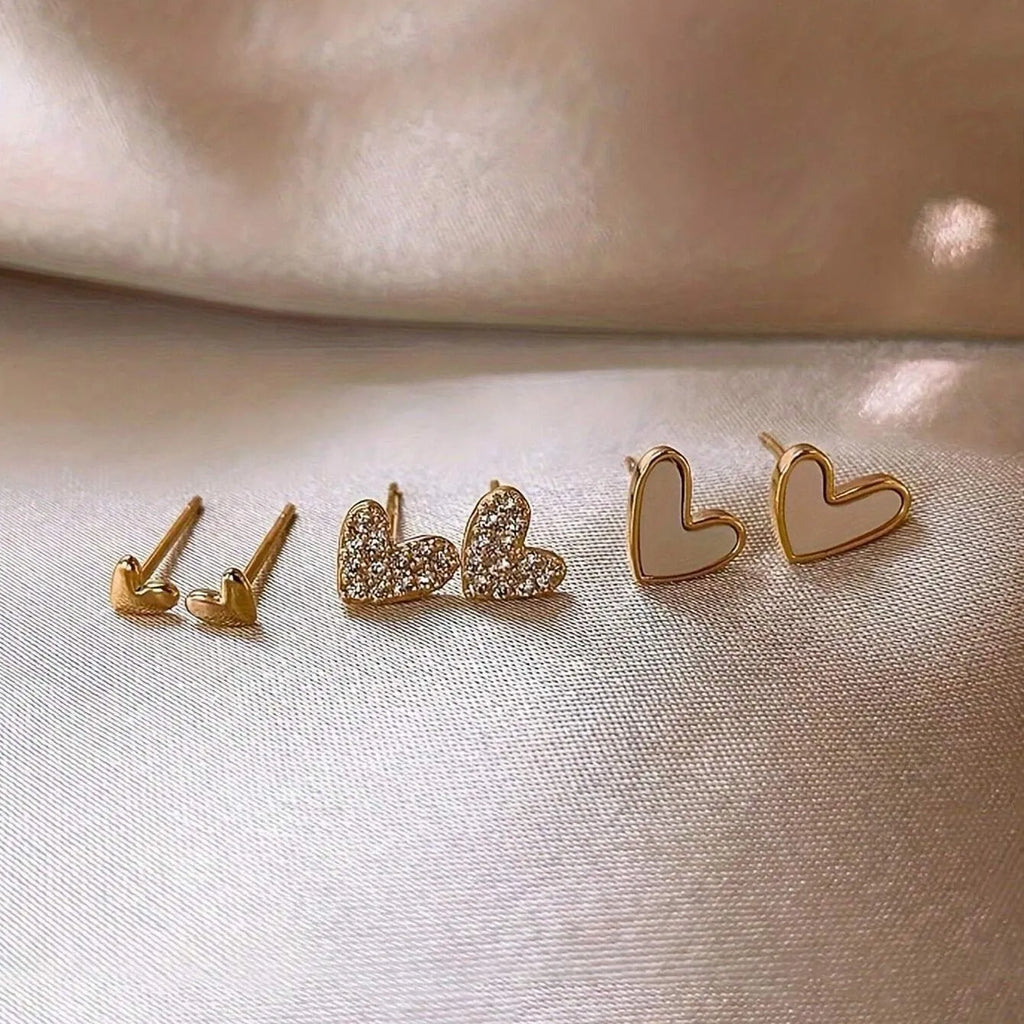 Three pairs of heart-shaped alloy earrings in gold, black, black and white, and pink colours with electroplated finish