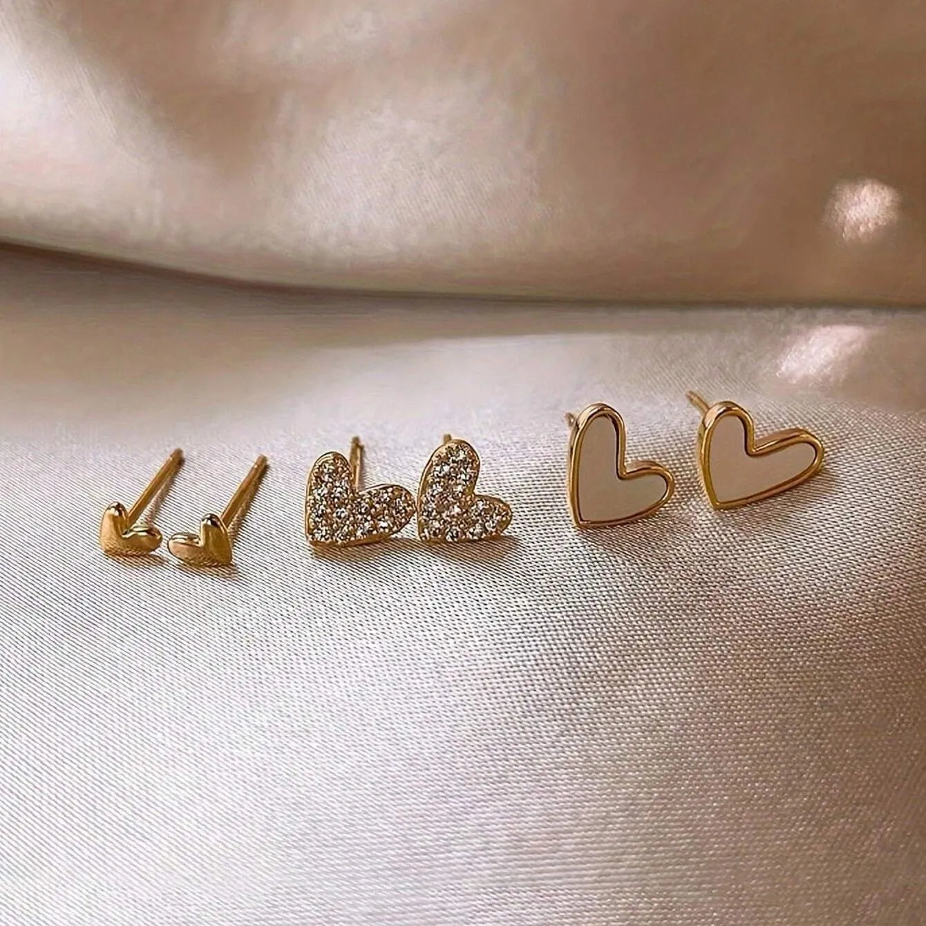 Three pairs of heart-shaped alloy earrings in gold, black, black and white, and pink colours with electroplated finish