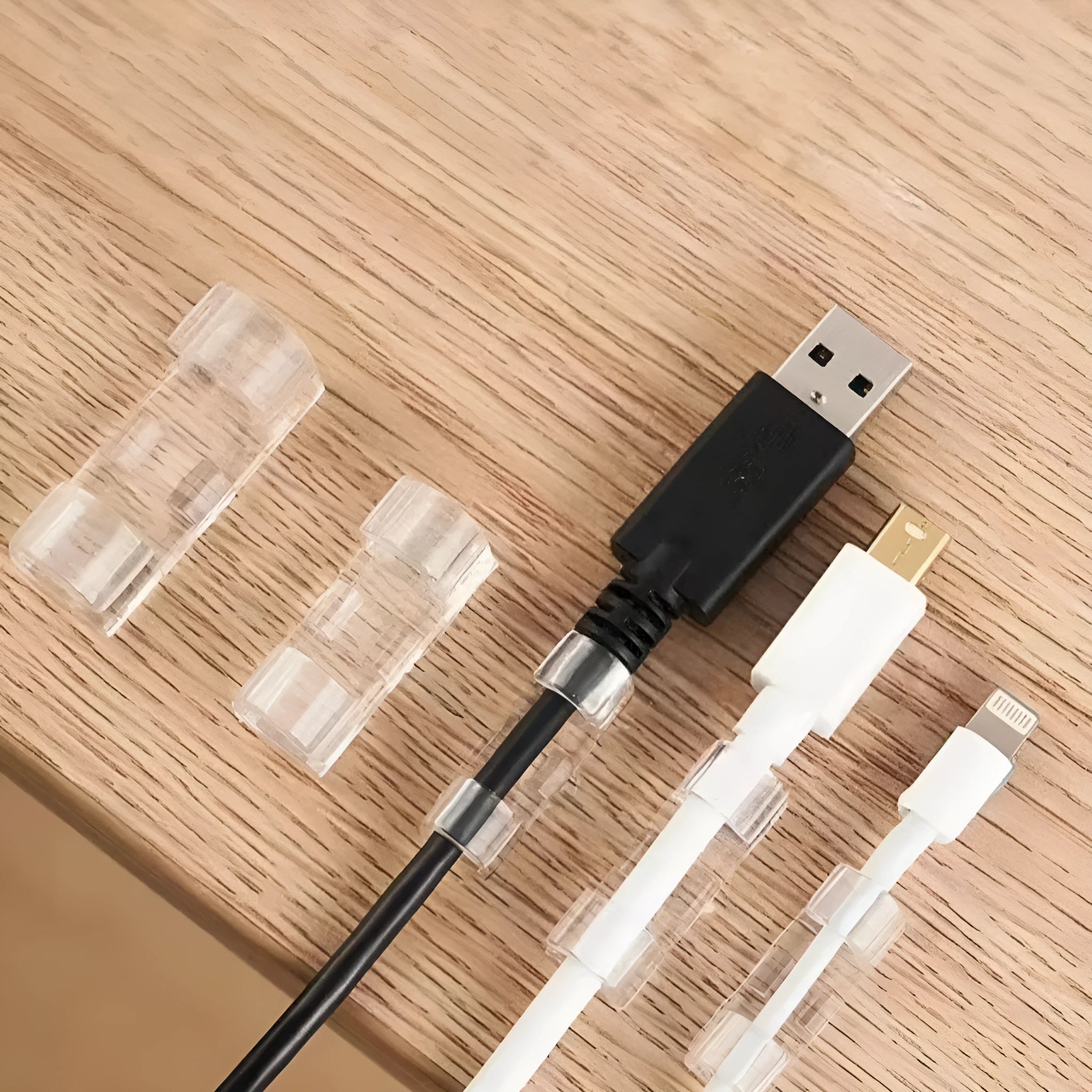 Transparent self-adhesive plastic wire holder snap clips for cable management on a white surface.