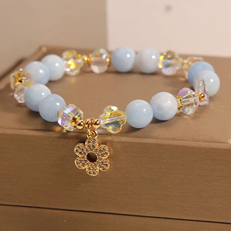Aquamarine crystal bracelet with four-leaf clover charm and pearl detail on a wrist.