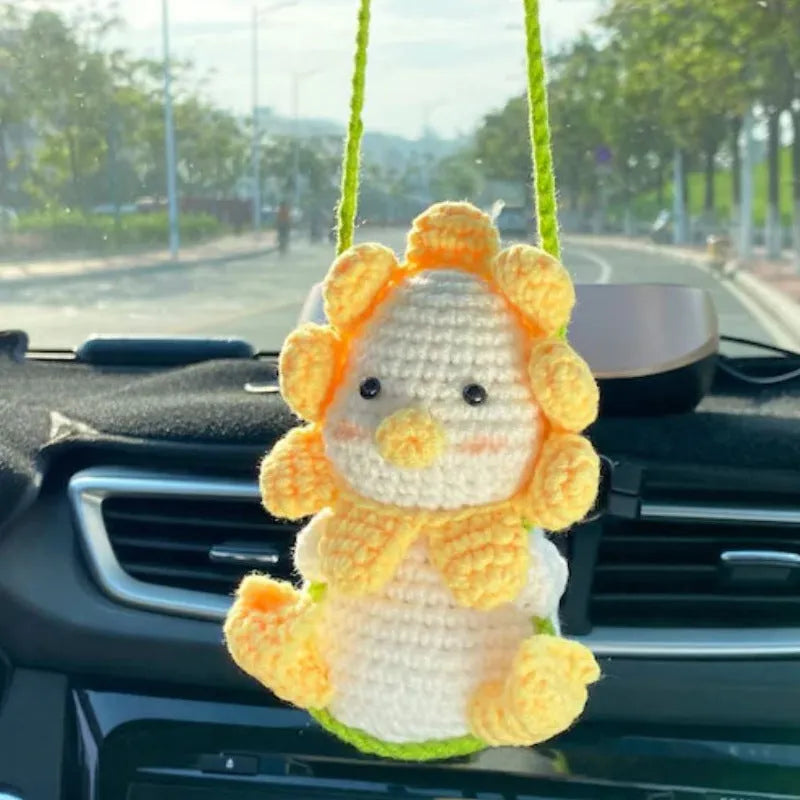 Green and white crocheted car plant decoration with hanging rope on a car dashboard.