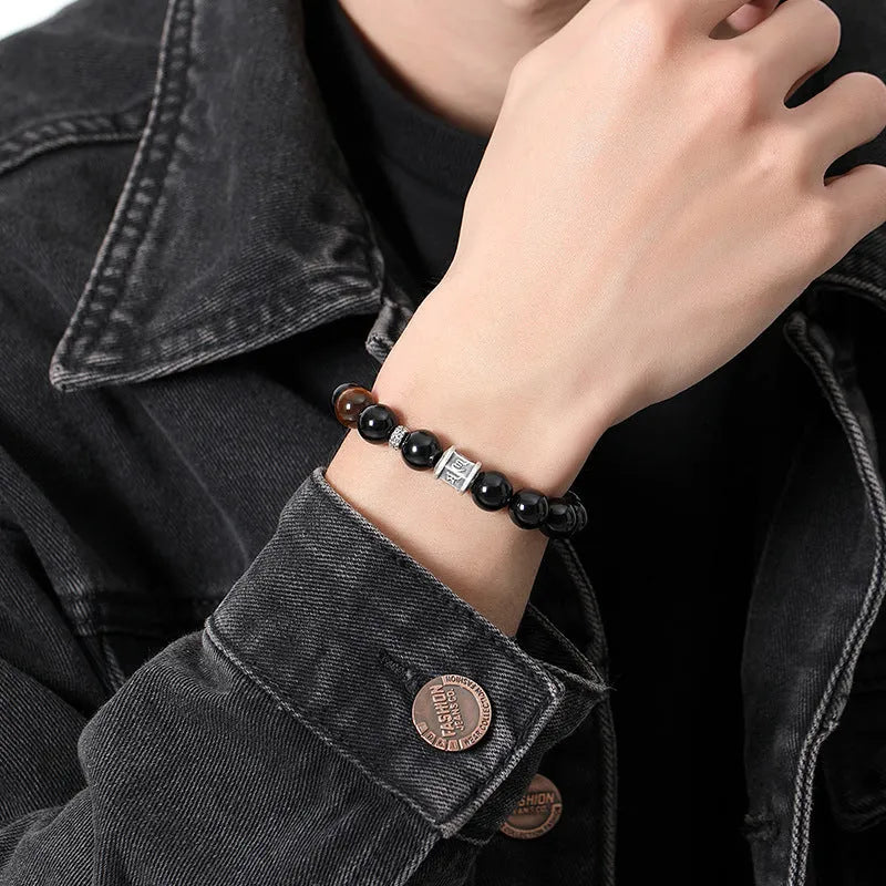 Men's black obsidian and silver bracelet with a 10mm prayer wheel charm on a dark background.