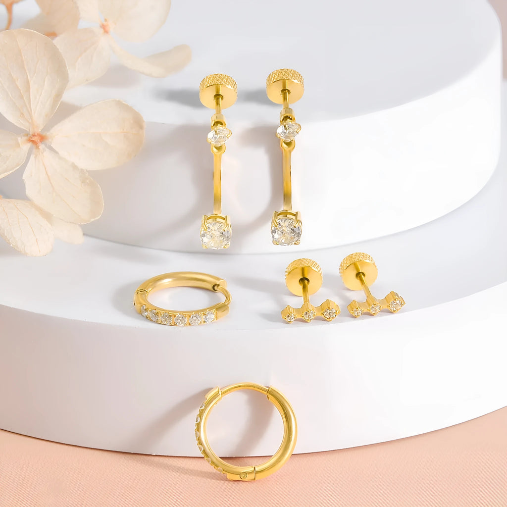 Three pairs of titanium steel ring-shaped geometric stud earrings with zircon inlay on a grey surface in steel and gold tones.
