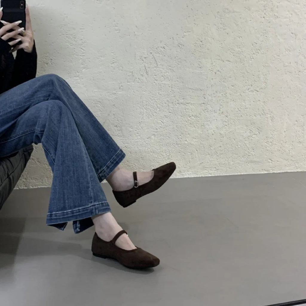 Women's black suede flat shoes with buckle closure and low heel on a neutral background