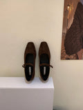 Women's black suede flat shoes with buckle closure and low heel on a neutral background