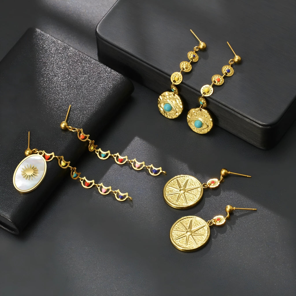 Geometric stainless steel drop earrings showing Eight Awn Star, Eye, and Shell Sun designs on a white background.