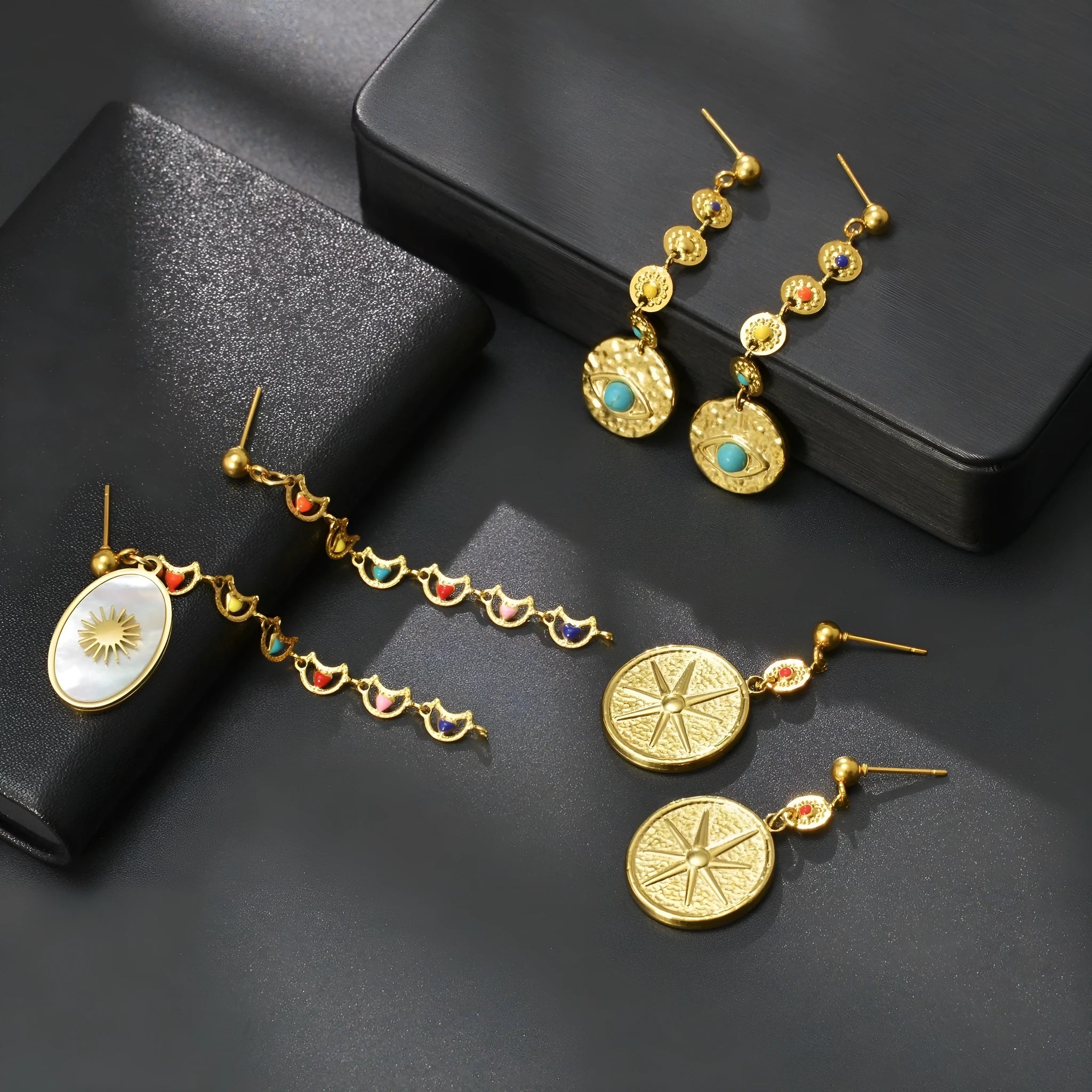 Geometric stainless steel drop earrings showing Eight Awn Star, Eye, and Shell Sun designs on a white background.