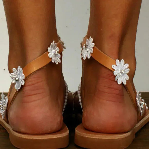 Brown women's Roman sandals with herringbone toe design and flower elements on flat rubber sole