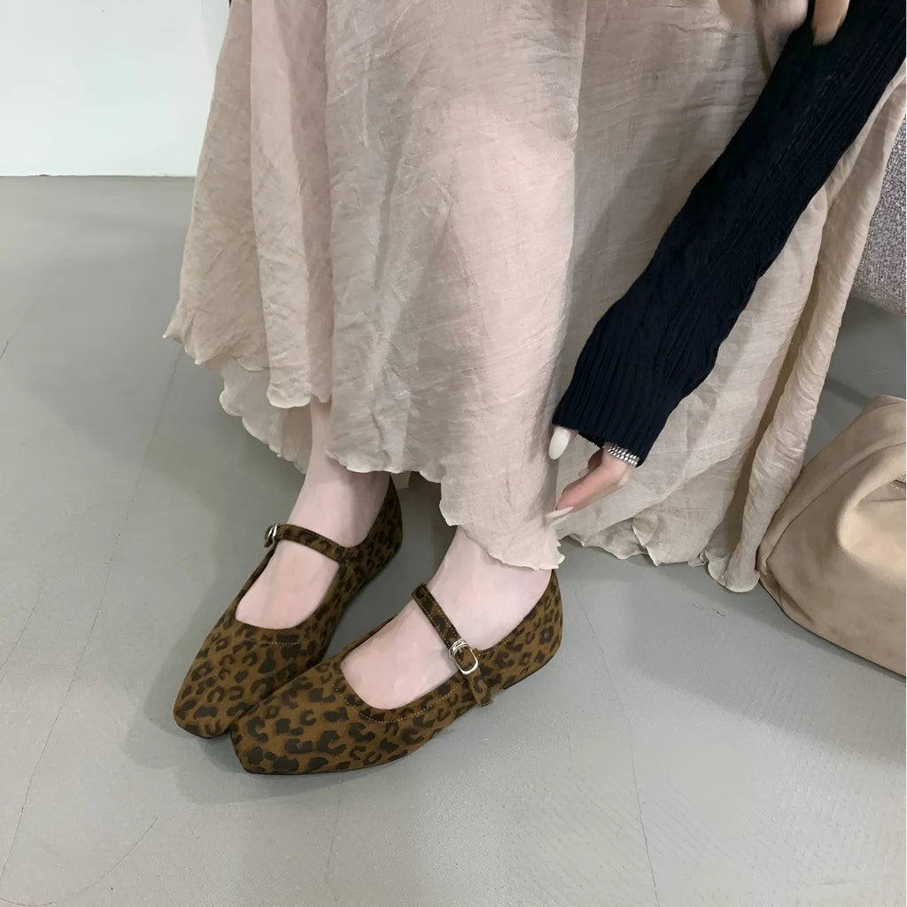 Women's black suede flat shoes with buckle closure and low heel on a neutral background
