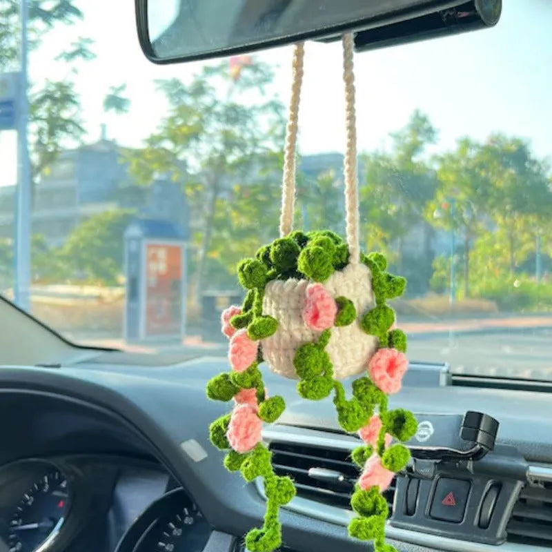 Green and white crocheted car plant decoration with hanging rope on a car dashboard.