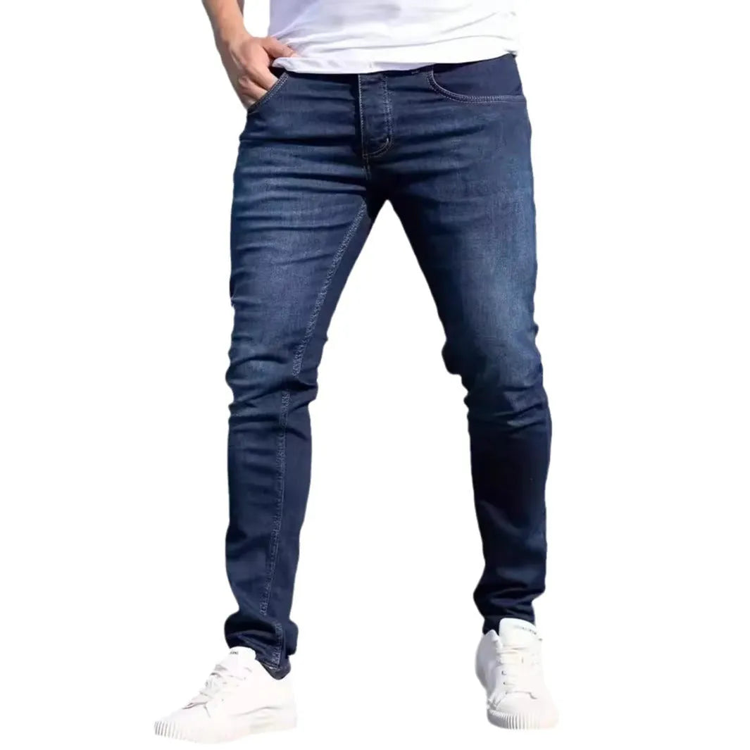 Dark blue men's skinny jeans with a mid-waist fit and zipper fly, laid flat.