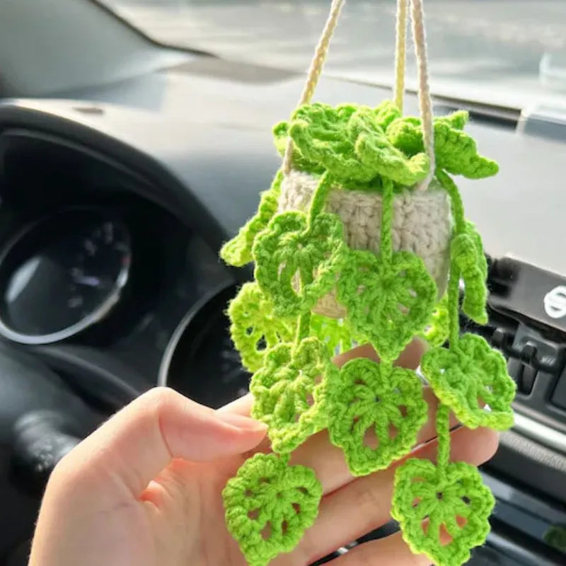 Green and white crocheted car plant decoration with hanging rope on a car dashboard.