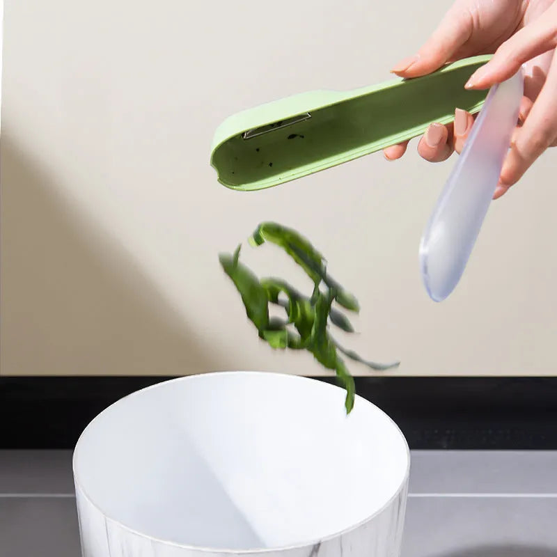 Dark green vegetable peeler with stainless steel blade inside its clear plastic storage tube on a kitchen counter.