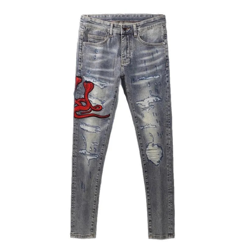 Close-up of distressed slim fit jeans showing worn wash, hole patches, and embroidery on blue denim.