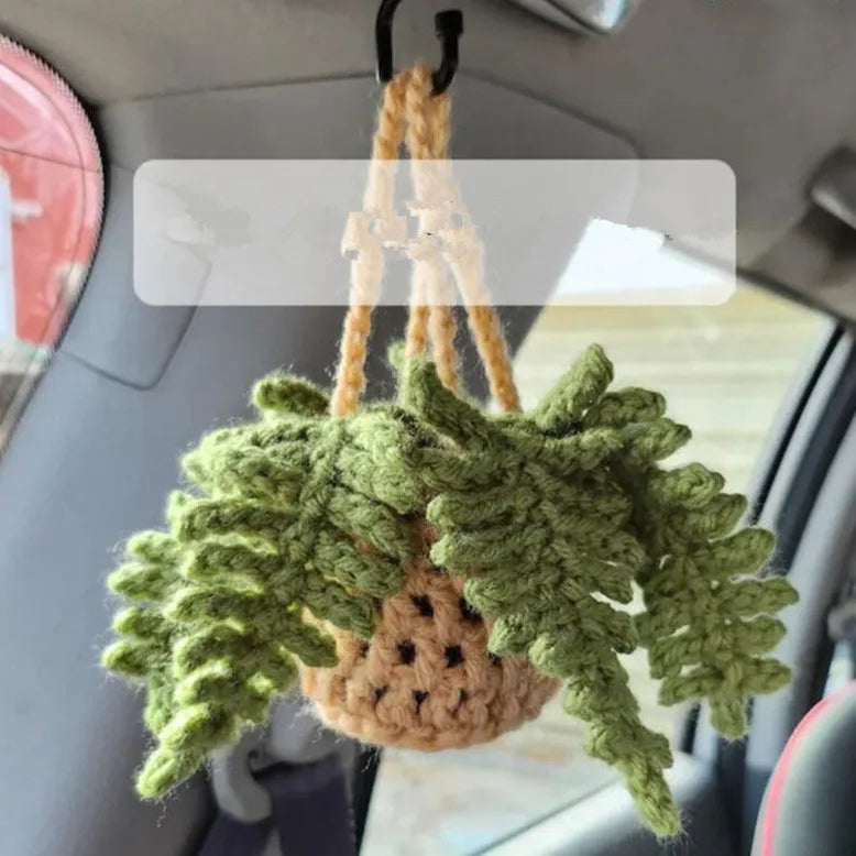 Green and white crocheted car plant decoration with hanging rope on a car dashboard.