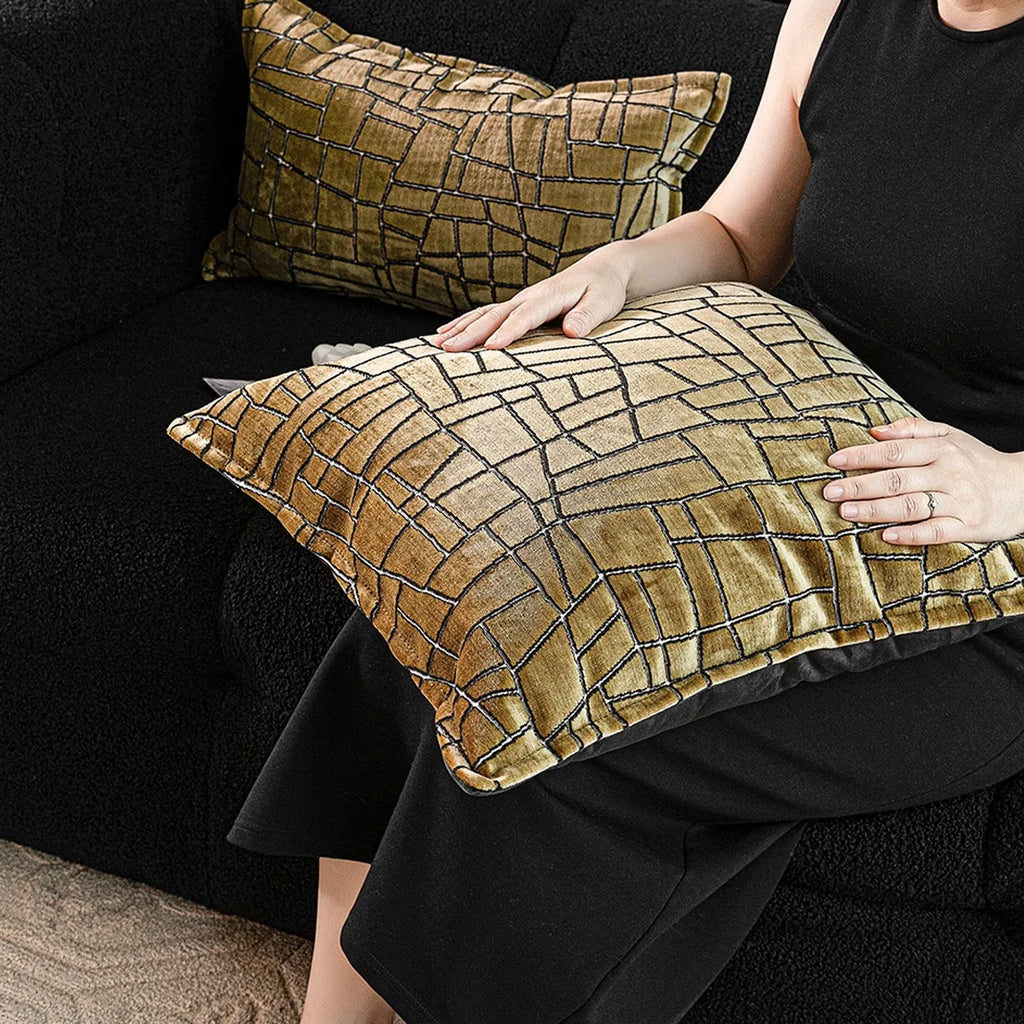 Gold geometric abstract patterned square cushion on a grey sofa.