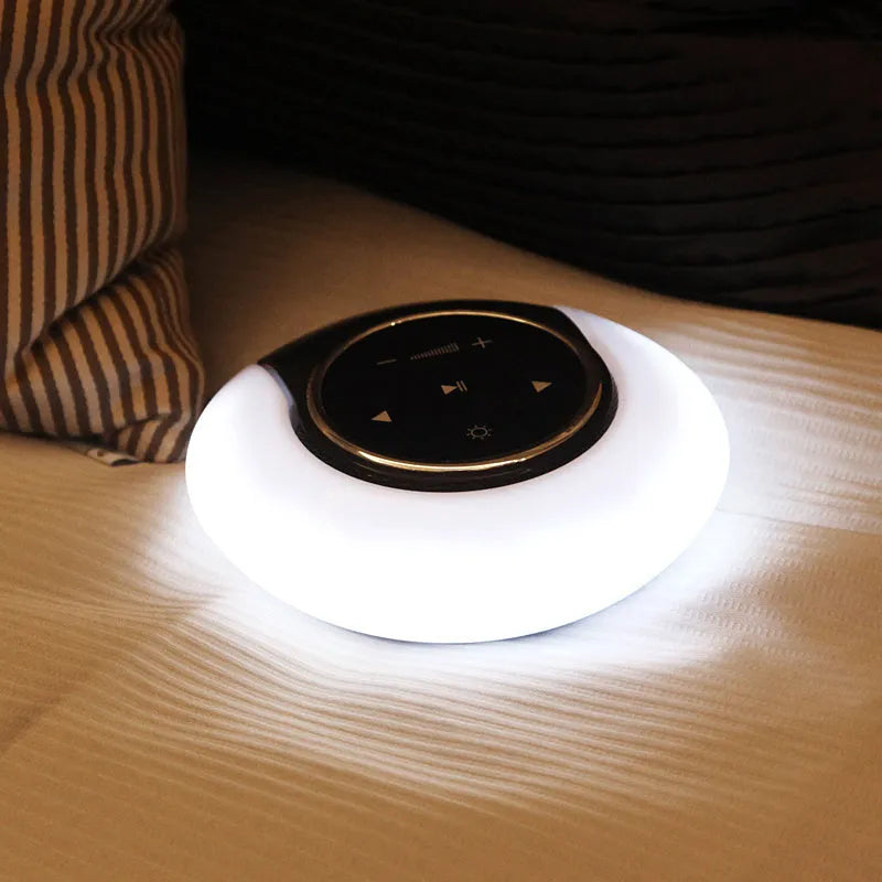 A blue and white foldable Bluetooth desk lamp with integrated speaker and touch controls on a wooden desk.