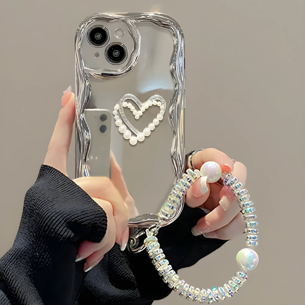 Silver grey silicone phone case for iPhone 15 Pro Max with three-dimensional pearls and chain, electroplated finish, and matching bracelet on a table