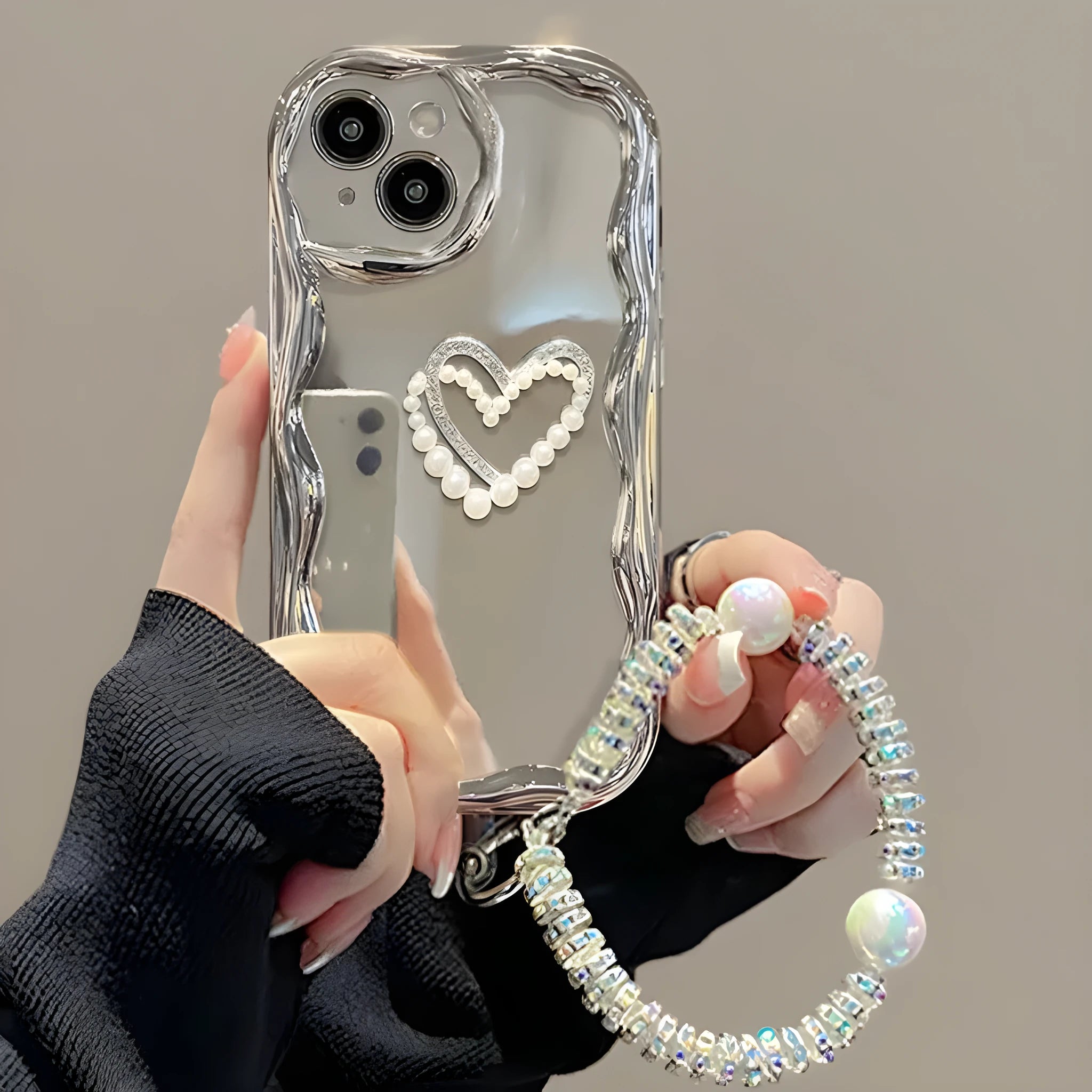 Silver grey silicone phone case for iPhone 15 Pro Max with three-dimensional pearls and chain, electroplated finish, and matching bracelet on a table