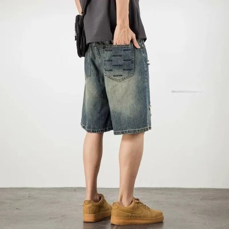 Blue men's distressed denim shorts with a loose, straight leg fit on a model.
