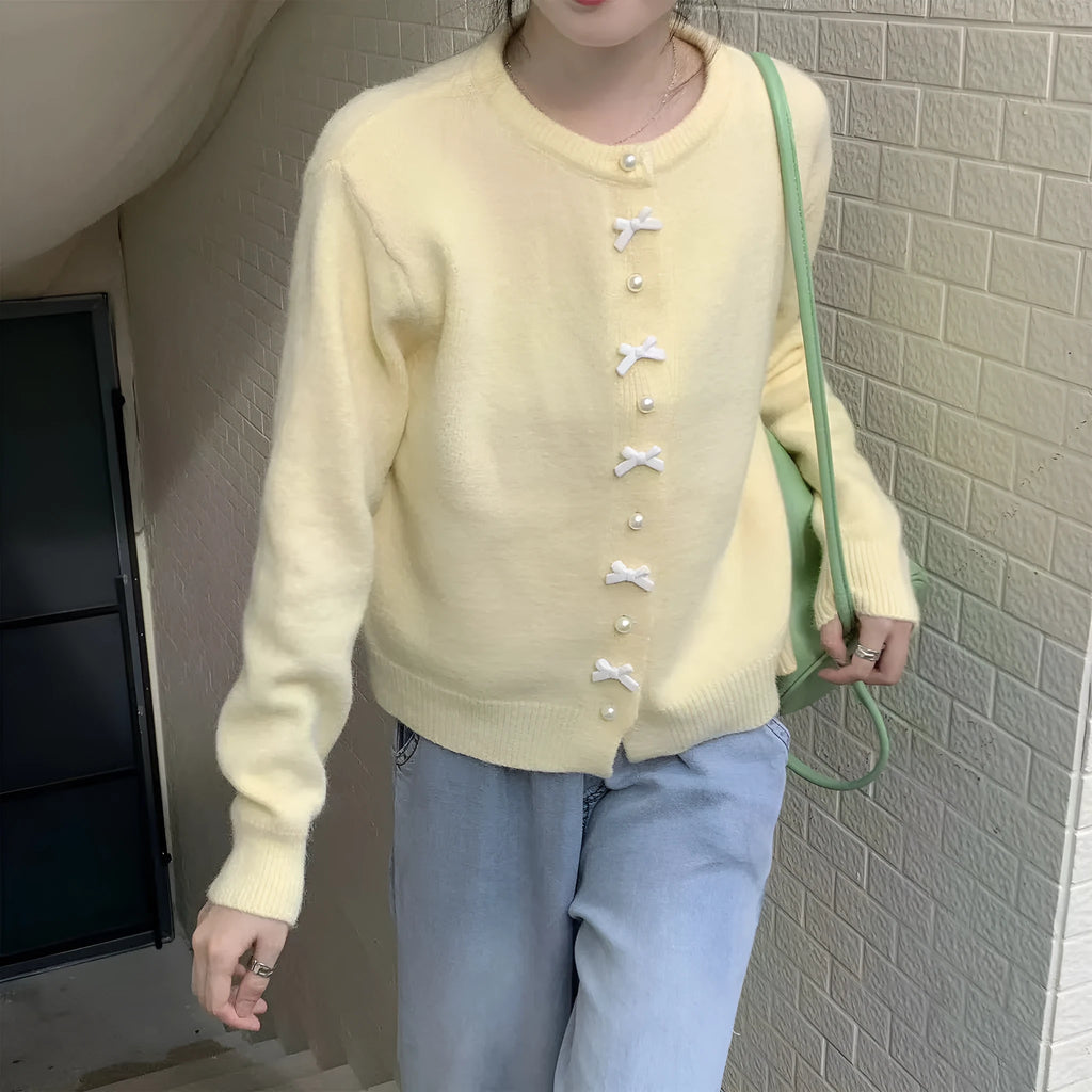 Women's light yellow cashmere acrylic cardigan with pearl buttons and a bow on the front.